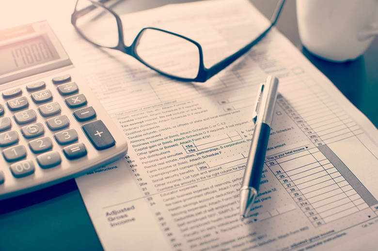 Tabela de impostos sobre mesa com uma calculadora, um óculos de grau e caneta em cima.