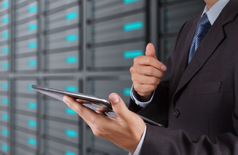 Homem em roupas sociais segurando um tablet em um datacenter.