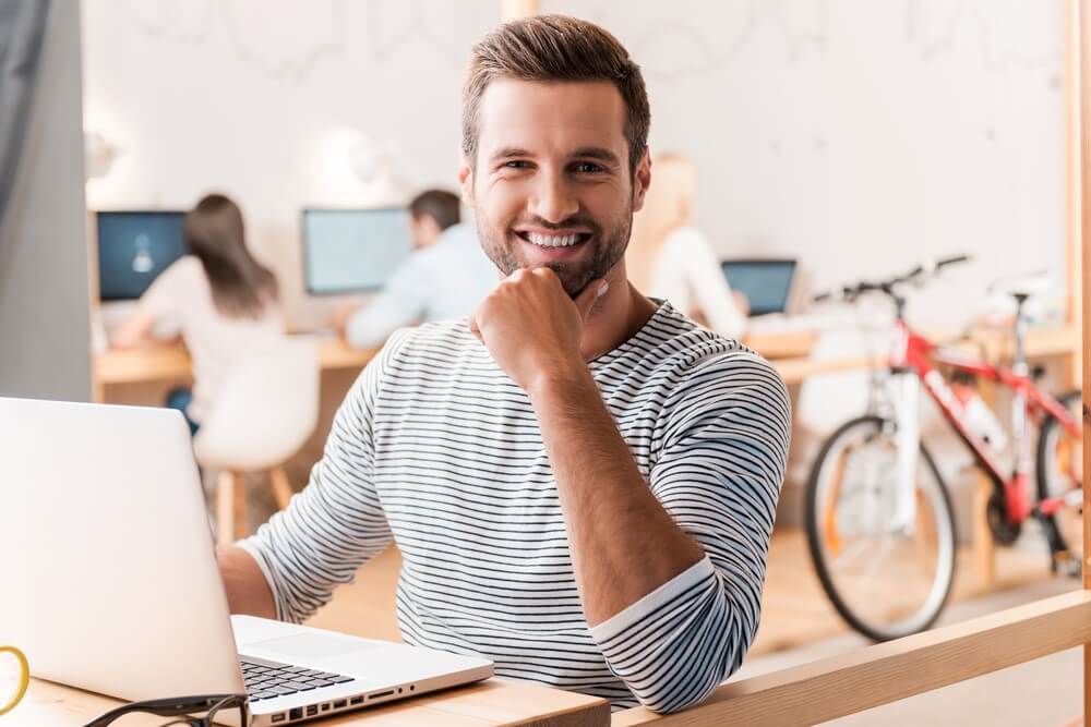 Homem caucasiano sentado em frente a computador sorri